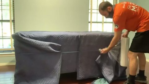 mover applying stretch wrap around a blanket-covered desk