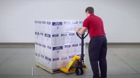 worker pushing a loaded pallet jack stacked with boxes