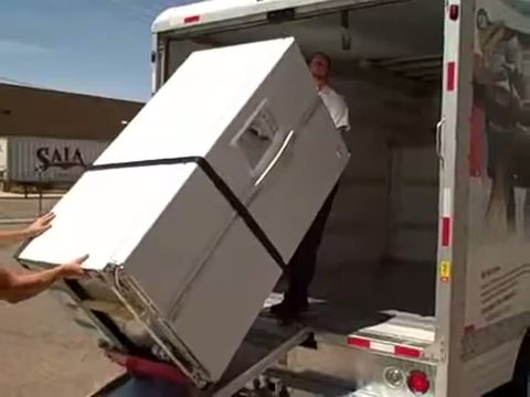 mover guiding a refrigerator on a hand truck into the back of a moving truck, face visible