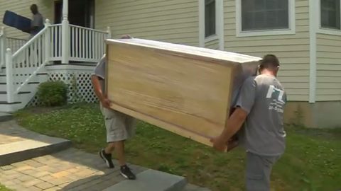 two movers carrying a large wood china cabinet across a front lawn