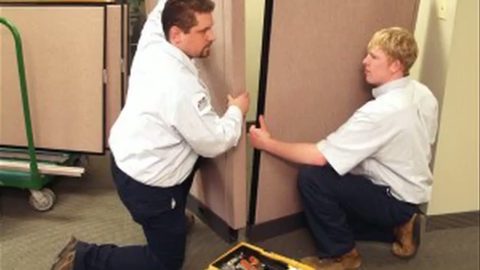two movers maneuvering office cubicle partition panels, face visible