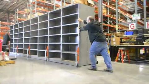 worker pushing a long run of warehouse shelving on caster jacks