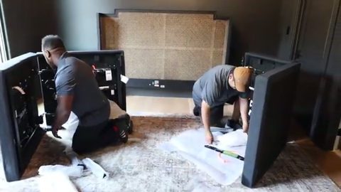 two movers padding disassembled furniture on a floor-protected rug