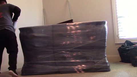 Mover tilts a blanket-wrapped dresser onto its side in a bedroom