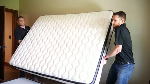 Two-man crew carrying a king mattress through a bedroom doorway, face visible